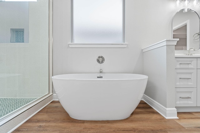 bathroom with a stall shower, vanity, a freestanding bath, and wood finished floors