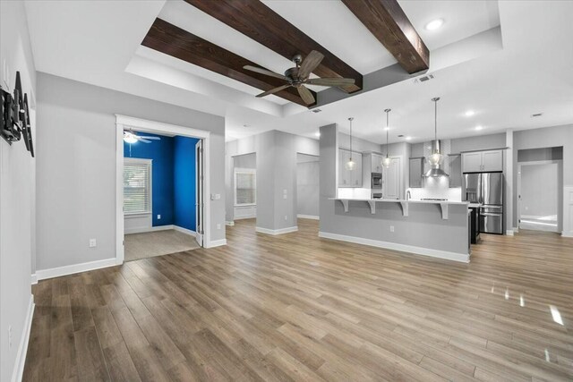 unfurnished living room with beam ceiling, a tray ceiling, ceiling fan, and light hardwood / wood-style flooring