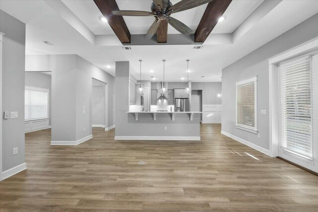 unfurnished living room featuring ceiling fan, beam ceiling, and light wood-type flooring