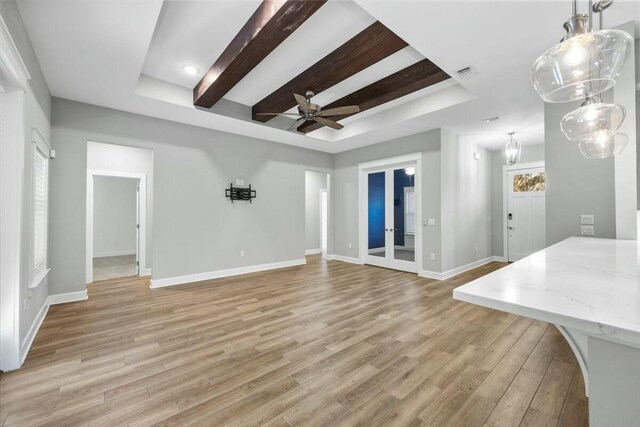 unfurnished living room with a tray ceiling, ceiling fan, and light hardwood / wood-style flooring