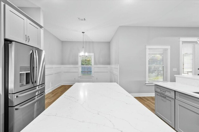 kitchen featuring hanging light fixtures, stainless steel refrigerator with ice dispenser, light stone countertops, and dark hardwood / wood-style flooring