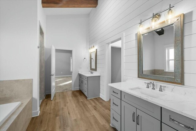 bathroom featuring vanity, wood-type flooring, tiled bath, and beam ceiling