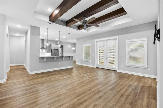 unfurnished living room with beamed ceiling, light wood-type flooring, ceiling fan, and a tray ceiling