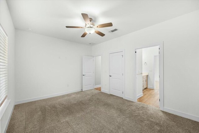 unfurnished bedroom with ceiling fan, ensuite bathroom, and light carpet