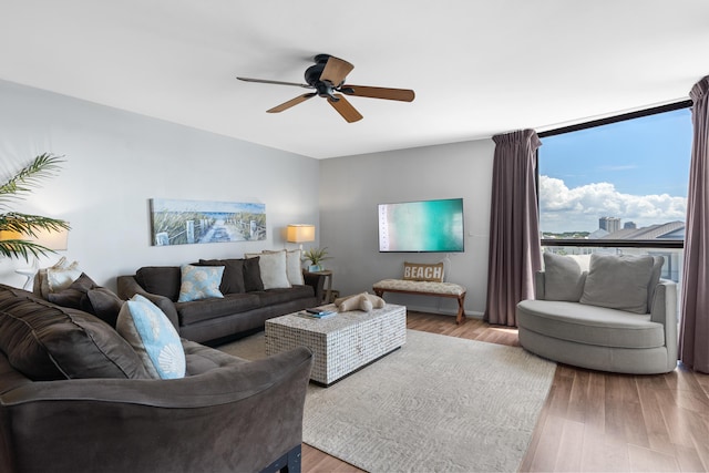 living room with a wall of windows, ceiling fan, and light wood-type flooring