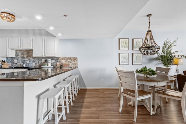 kitchen with decorative backsplash, kitchen peninsula, pendant lighting, an inviting chandelier, and white cabinets