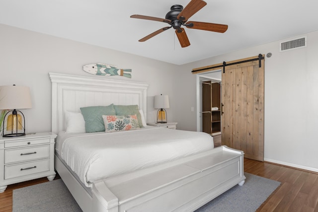 bedroom featuring ceiling fan, a barn door, and dark hardwood / wood-style floors