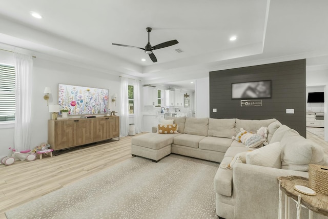 living room featuring light wood-type flooring, a raised ceiling, and ceiling fan