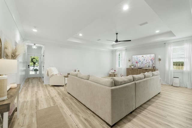 living room featuring light wood-type flooring, a raised ceiling, ceiling fan, and a healthy amount of sunlight