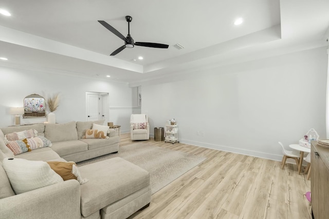 living room featuring light hardwood / wood-style floors, a raised ceiling, and ceiling fan