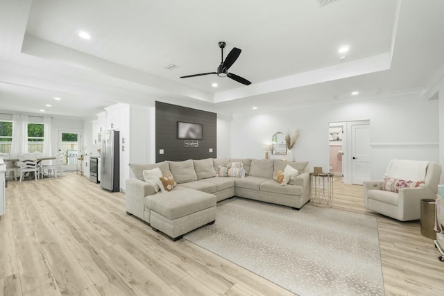 living room with ceiling fan, light wood-type flooring, ornamental molding, and a tray ceiling