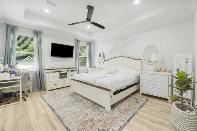 bedroom with a tray ceiling, ceiling fan, and light hardwood / wood-style flooring