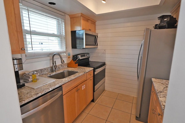 kitchen with wood walls, sink, light tile patterned floors, light stone counters, and stainless steel appliances