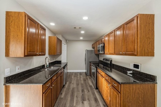 kitchen featuring wood-type flooring, appliances with stainless steel finishes, dark stone countertops, and sink