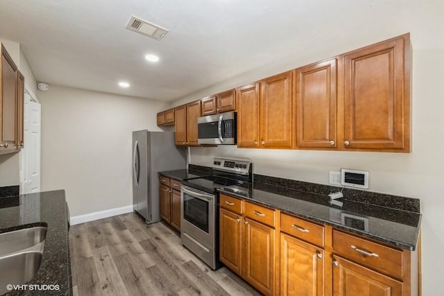 kitchen featuring appliances with stainless steel finishes, light hardwood / wood-style floors, dark stone counters, and sink