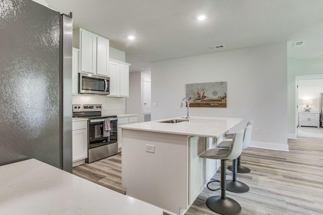 kitchen with white cabinets, a kitchen island with sink, sink, and appliances with stainless steel finishes