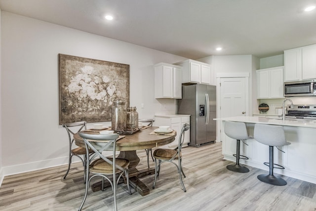 kitchen featuring a kitchen bar, stainless steel appliances, white cabinetry, and light hardwood / wood-style floors