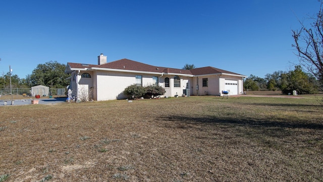 rear view of property featuring a lawn, a shed, and a garage