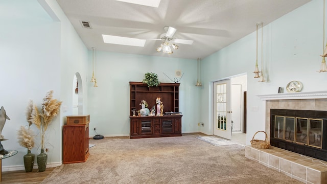 interior space featuring carpet flooring, ceiling fan, a tile fireplace, and a skylight