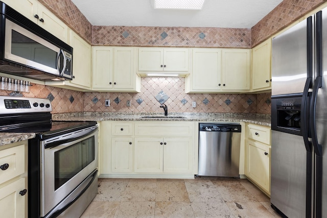 kitchen featuring light stone countertops, appliances with stainless steel finishes, cream cabinets, and sink