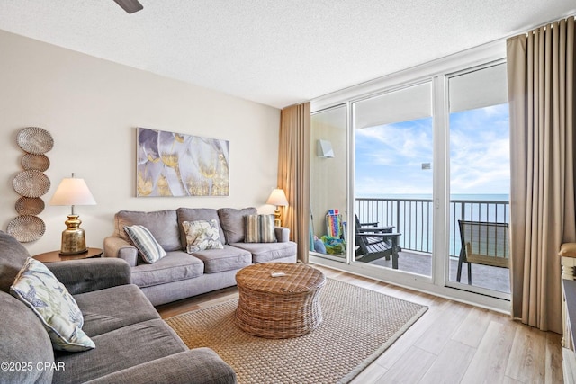 living room featuring light wood-type flooring, a textured ceiling, a water view, and expansive windows