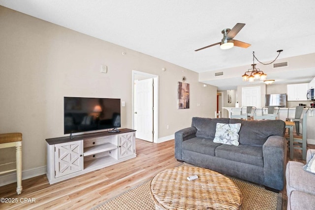 living room featuring ceiling fan with notable chandelier and light wood-type flooring