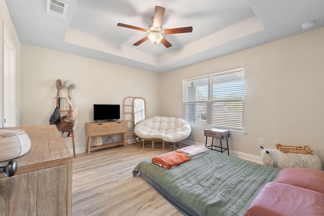 bedroom featuring light wood-type flooring, a raised ceiling, and ceiling fan