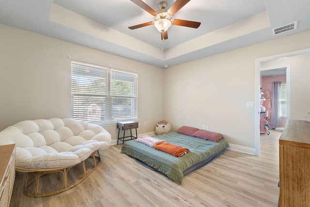 bedroom featuring a raised ceiling, ceiling fan, and light hardwood / wood-style flooring