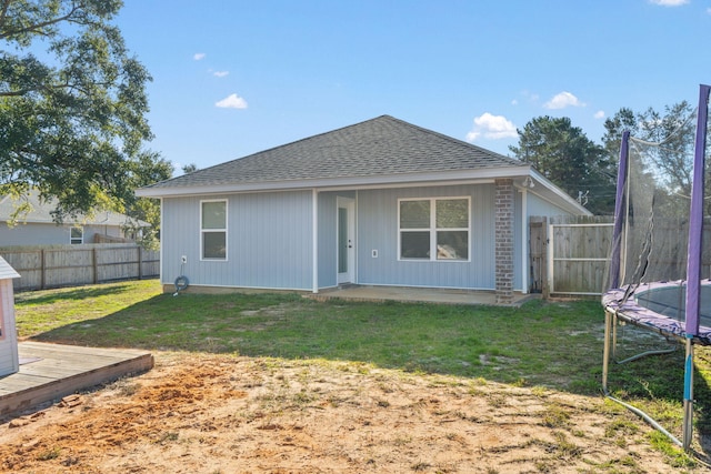 rear view of property featuring a lawn and a trampoline