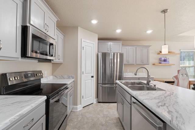 kitchen featuring appliances with stainless steel finishes, light stone counters, a textured ceiling, sink, and decorative light fixtures