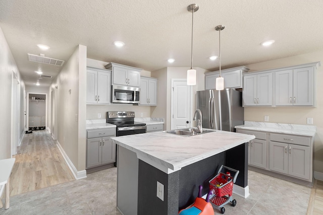 kitchen featuring appliances with stainless steel finishes, gray cabinetry, a kitchen island with sink, sink, and decorative light fixtures