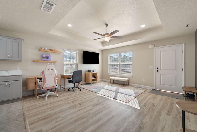 office space with a textured ceiling, light hardwood / wood-style floors, a raised ceiling, and ceiling fan