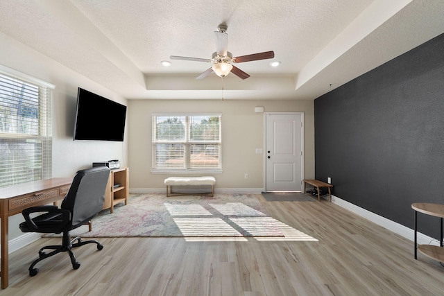 office area featuring a tray ceiling, ceiling fan, a textured ceiling, and light wood-type flooring