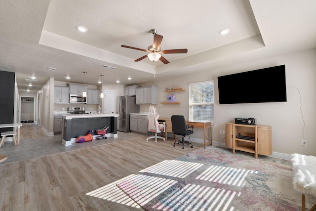 living room featuring light hardwood / wood-style flooring, a raised ceiling, ceiling fan, and sink