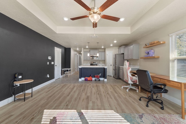 office area with ceiling fan, light wood-type flooring, a textured ceiling, and a tray ceiling