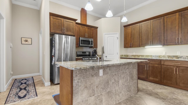 kitchen featuring light stone counters, stainless steel appliances, crown molding, pendant lighting, and an island with sink