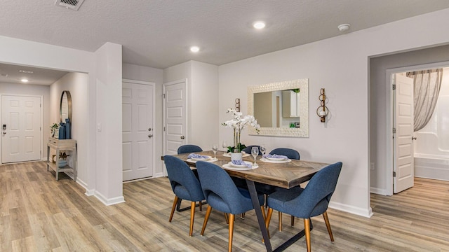 dining area featuring light wood-type flooring and a textured ceiling