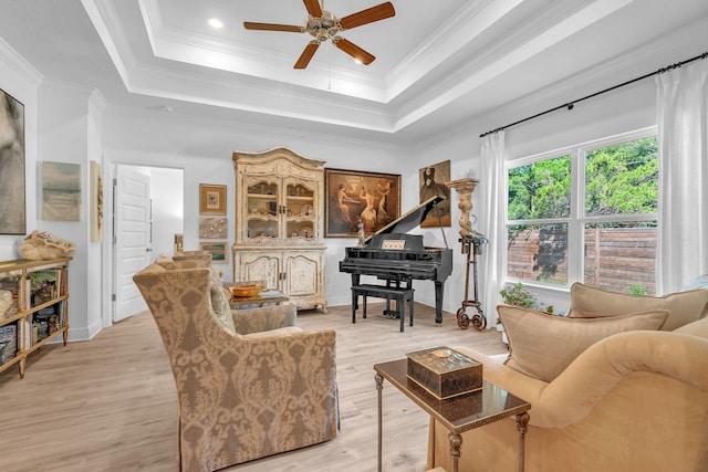 living room with light hardwood / wood-style floors, ceiling fan, crown molding, and a tray ceiling