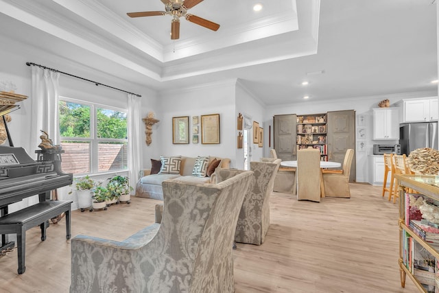 living room featuring ceiling fan, light wood-type flooring, and a tray ceiling