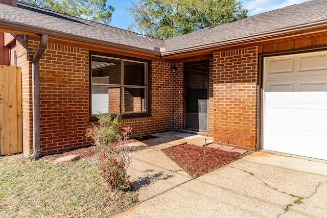 doorway to property with brick siding, an attached garage, and a shingled roof