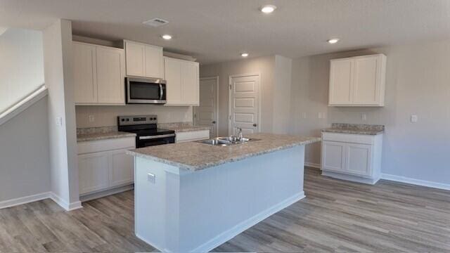 kitchen with sink, light hardwood / wood-style floors, a center island with sink, white cabinets, and appliances with stainless steel finishes