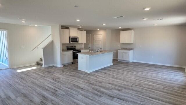 kitchen with light hardwood / wood-style floors, white cabinetry, stainless steel appliances, and an island with sink