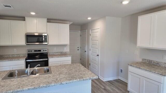 kitchen with light stone countertops, stainless steel appliances, white cabinetry, and sink