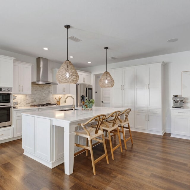 kitchen featuring sink, stainless steel appliances, wall chimney range hood, decorative light fixtures, and white cabinets