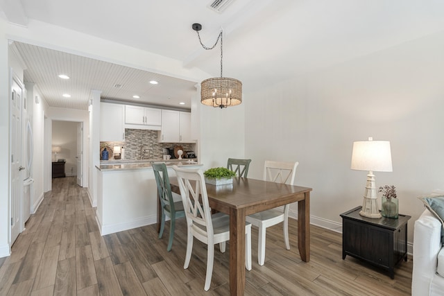 dining room featuring beam ceiling, sink, light hardwood / wood-style flooring, and a notable chandelier