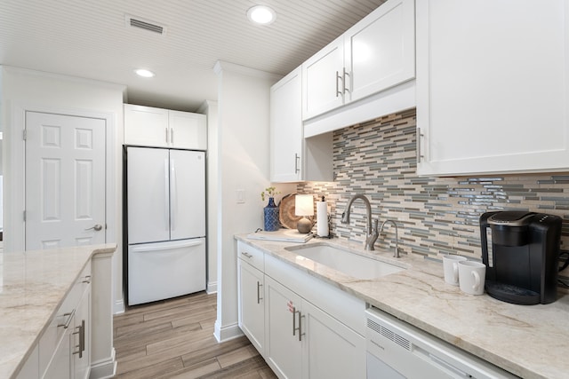 kitchen featuring sink, white cabinetry, white refrigerator, light stone countertops, and backsplash