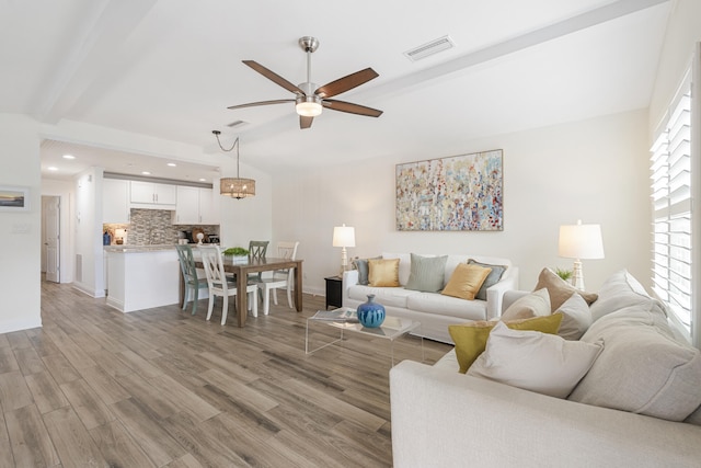 living room with light hardwood / wood-style flooring, beamed ceiling, and ceiling fan