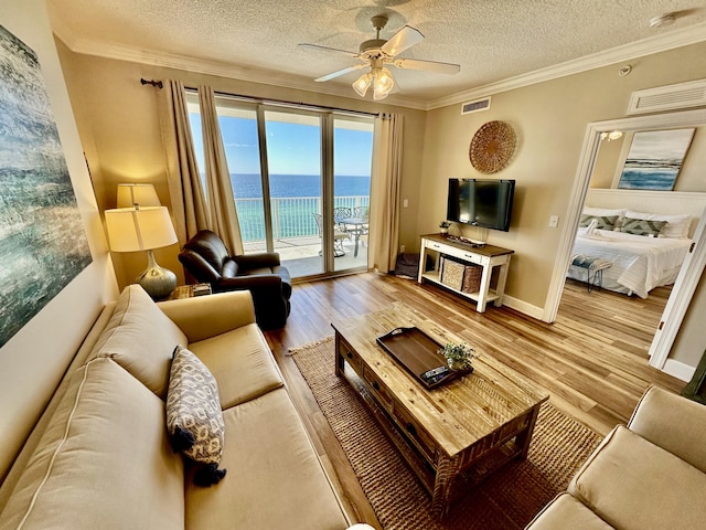 living room featuring ceiling fan, light hardwood / wood-style floors, ornamental molding, and a textured ceiling