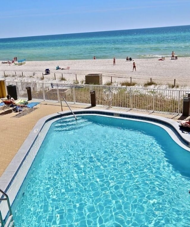 view of swimming pool featuring a water view, a patio, and a view of the beach