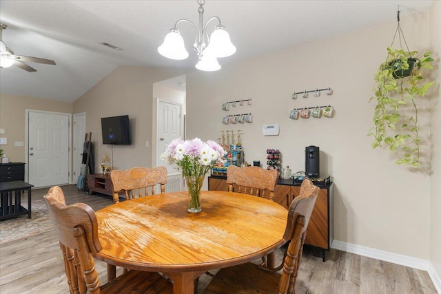 dining area with light wood-type flooring, ceiling fan with notable chandelier, and vaulted ceiling